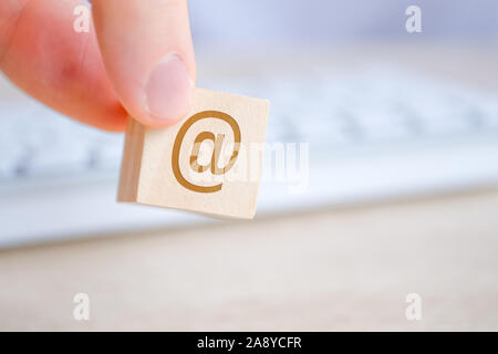 A man hand holds a wooden cube with the image of an email symbol. Concept of contacts for communication over the Internet. Close up. Stock Photo