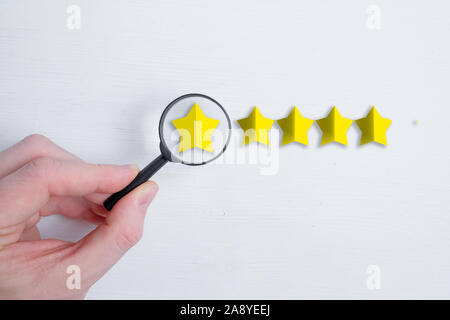 A man holds a glass like magnifier over an abstract five stars rating on a white background. Grade Analysis Concept. Best score. Flat lay. Close up. Stock Photo