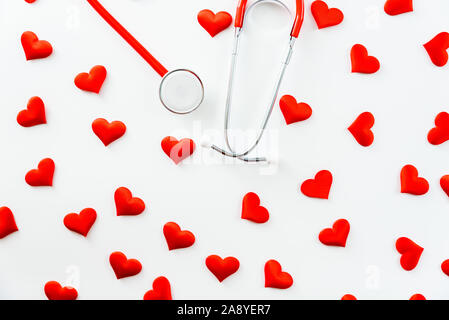 Stethoscope isolated on simple white background viewed from above surrounded by red hearts. Stock Photo