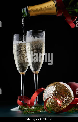 Christmas and New Years Eve celebration concept: two glasses full of bubbly drink and a bottle of champagne on a table with Christmas decorations. Stock Photo