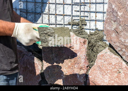 Builder - mason hands placing stones on a wall using a spatula with cement, outdoors Stock Photo