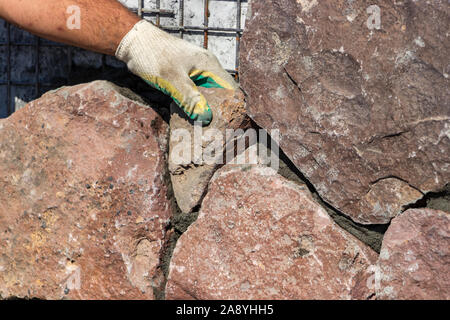 Builder - mason hands placing stones on a wall using cement, outdoors Stock Photo
