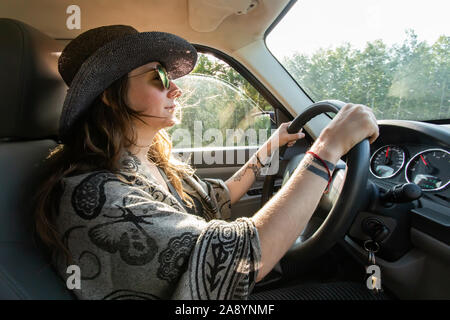 Young woman driving her big SUV. General view of cabin from the sideways. Woods and green environment at backgorund. Lifestyle. Stock Photo