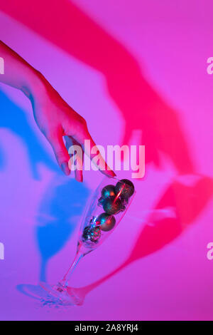 the female hand coquettishly holds a glass of champagne filled with New Year's balls. Photo in trendy neon color. new year concept Stock Photo