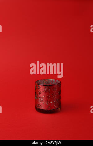 glass candlestick with ornament of snowflakes on a red background. Vertical photo. Copy space. Christmas concept. Minimalism. Stock Photo