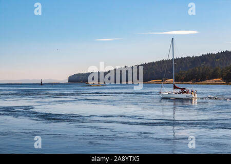 Under an almost cloudless sky, a sailboat motors through tidal whirlpools at Gabriola Passage, British Columbia (Valdes Island in background). Stock Photo