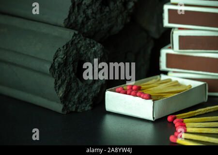 Box of matches and Carbon activated bamboo charcoal on dark background. Concept of fuel for living in the forest. Closeup and copy space. Stock Photo
