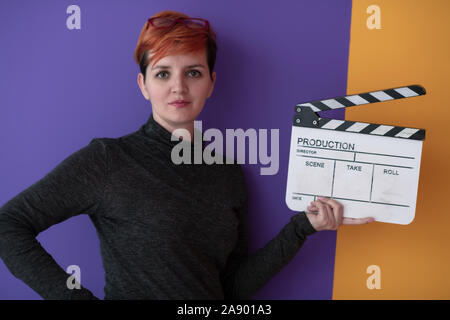 redhead woman holding movie clapper against purple  background  cinema concept Stock Photo