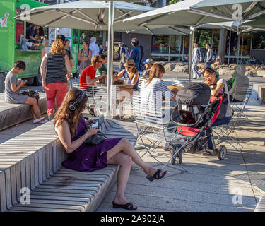 Students sitting outside  at tables in Harvard Square, some using mobile phones Stock Photo