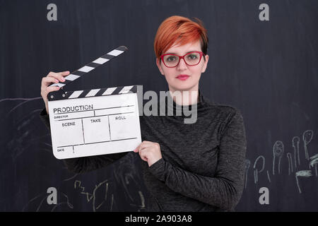 redhead woman on black chalkboard holding movie clapper cinema concept Stock Photo