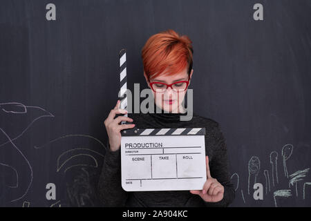 redhead woman on black chalkboard holding movie clapper cinema concept Stock Photo