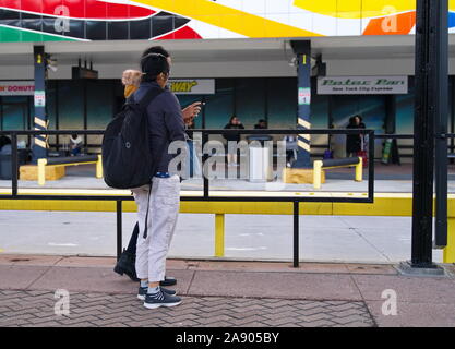 Hartford, CT USA. Oct 2019. Young women at the bus stop checking travel scheduling on smartphone. Stock Photo