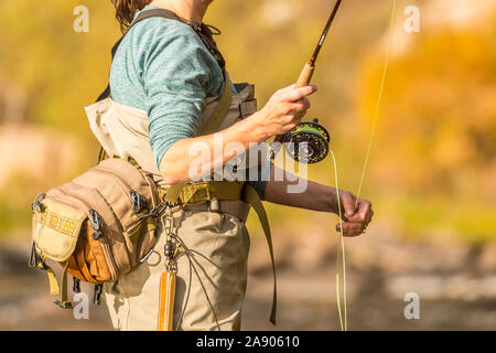 A woman holds her fly rod and reel while fishing on a sunny fall afternoon in Northern Colorado. Stock Photo