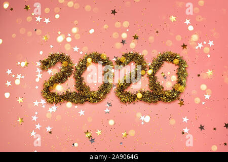 2020 new year gold numbers on a coral color background with scattered stars and bokeh lights Stock Photo