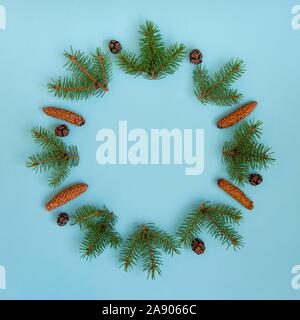 A wreath of pine tree branches and cones over blue background. Stock Photo