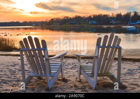 Two white Adirondack chairs on a lawn overlooking the Atlantic Ocean