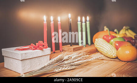 Kwanzaa holiday concept with decorate seven candles red, black and green, gift box, pumpkin,corn and fruit on wooden desk and background. Stock Photo