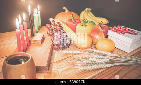 Kwanzaa holiday concept with decorate seven candles red, black and green, gift box, pumpkin,corn and fruit on wooden desk and background. Stock Photo