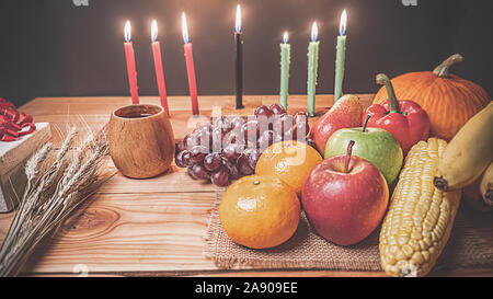 Kwanzaa holiday concept with decorate seven candles red, black and green, gift box, pumpkin,corn and fruit on wooden desk and background. Stock Photo