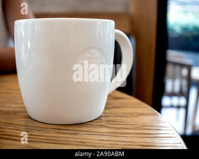 SEPTEMBER 28, 2019 : Bangkok, Thailand : White Starbucks coffee mug with low relief logo on wooden table in Starbucks cafe, Starbucks is the largest c Stock Photo