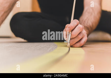 The worker primes the joint between the tile and the parquet on the floor before installing the cork grouser Stock Photo