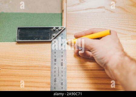 The carpenter marks the smooth cutting line on the board with the help of a construction square and a pencil Stock Photo