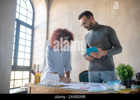 Bearded interior designer watching trainee making sketches Stock Photo