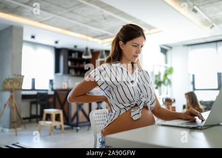 Tired pregnant woman working from home on computer Stock Photo