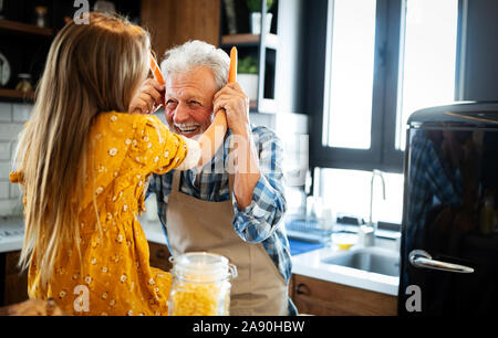 Happy young girl and her grandfather cooking together in kitchen Stock Photo