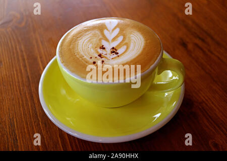 Closeup cappuccino coffee with latte art in a yellow cup on wooden table Stock Photo