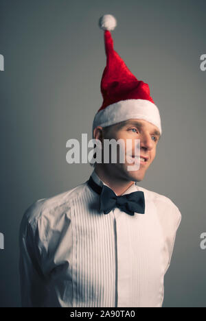 Portrait of young man in formal black tie tuxedo swinging his Santa hat with a smile Stock Photo