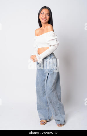 Full body shot of happy young beautiful Asian woman looking over shoulder Stock Photo