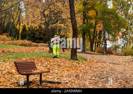 Worker in autumn park with a leaf blower Stock Photo