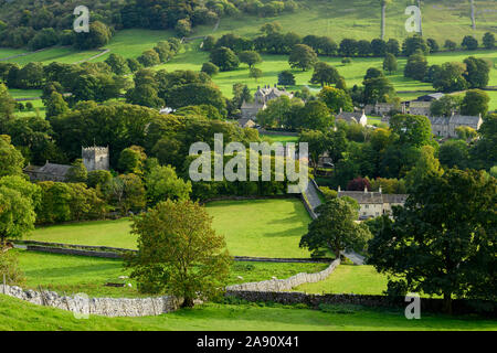 Summer evening sunlight on picturesque Dales village (church & houses) nestling in valley under upland hills - Arncliffe, North Yorkshire, England, UK