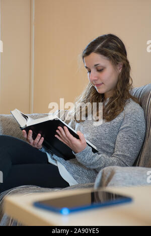 Young caucasian girl reads a happy book ignoring her smartphone. Concept of love towards books Stock Photo