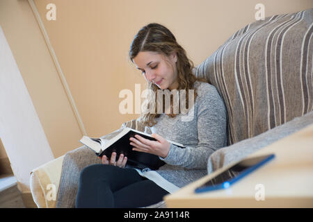 Young caucasian girl reads a happy book ignoring her smartphone. Concept of love towards books Stock Photo