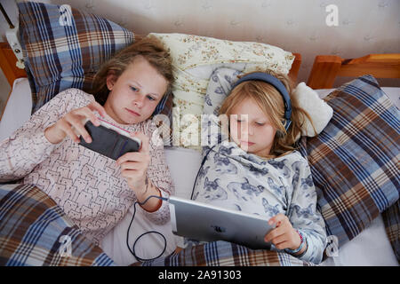 Sisters on bed using digital devices Stock Photo