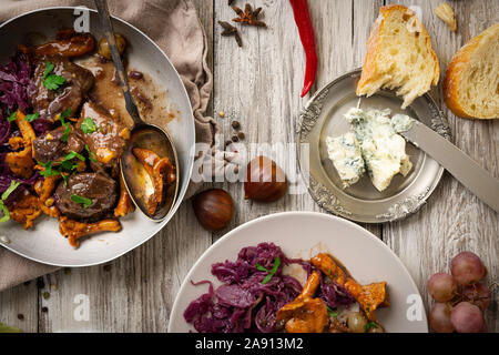 venison dish on old wooden table, with fruits jam, cheese and chestnuts, traditional winter dish with meat, hunting loot Stock Photo