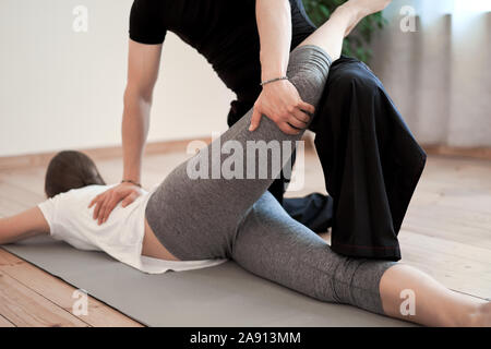 Brunette woman doing stretching on mat with male trainer in gym Stock Photo