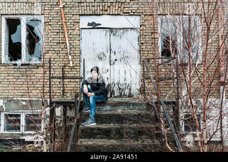 Teenage boy sitting at steps of abandoned building Stock Photo