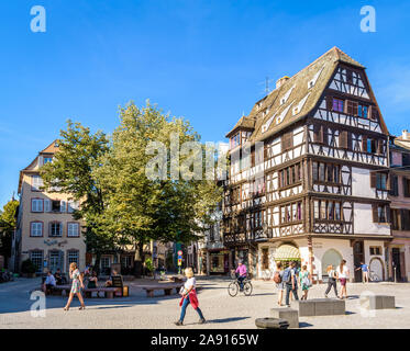 People strolling and cycling on the Saint-Etienne square, lined with half-timbered buildings, in the historic district of Strasbourg, France. Stock Photo