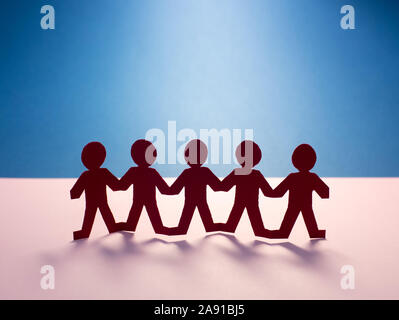 Team of paper chain people in a row on paper background holding hands Stock Photo