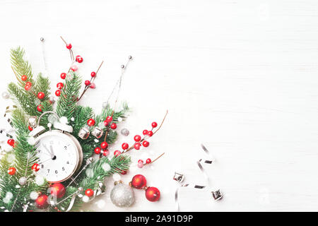 Christmas clock, fir branches and berries on white wooden background. New Year greeting card. Stock Photo
