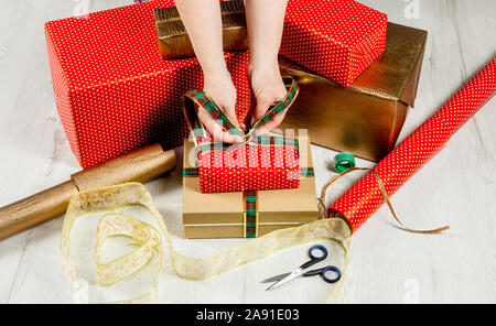 Close up view of woman wrapping Christmas gifts in paper. Lot of boxes, ribbons, scissors, tape on white wood floor. Stock Photo