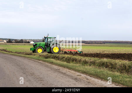 Wheel tractor with a plow, leaves the field on an asphalt road. Plowing the land in late autumn. Podlasie, Poland. Stock Photo