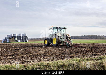 Wheel tractor with multi-plow, plowing the field. Bales of silage in the background. Plowing the land in late autumn. Podlasie, Poland. Stock Photo