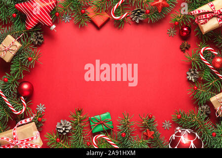 Christmas frame made of fir branches, gift boxes, red holiday decorations and candy on red background. Christmas or Happy New Year concept. Flat lay. Stock Photo