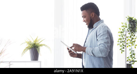 Smiling african man using digital tablet while standing near window Stock Photo