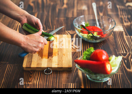 Young woman is cutting cucumber on cutting board for salad. Stock Photo