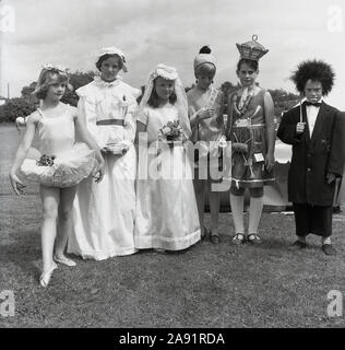 1967, historical, children line up in their costumes for the fancy dress compeition at Speen fete, England, UK. We have a variety of costumes on show, including a ballet dancer, a bride, and a Miss Ascot. The young girl wearing cotton strands on her dress and a straw hat is fun but not sure who the young boy on the right is meant to be, but love the teeth!. Stock Photo